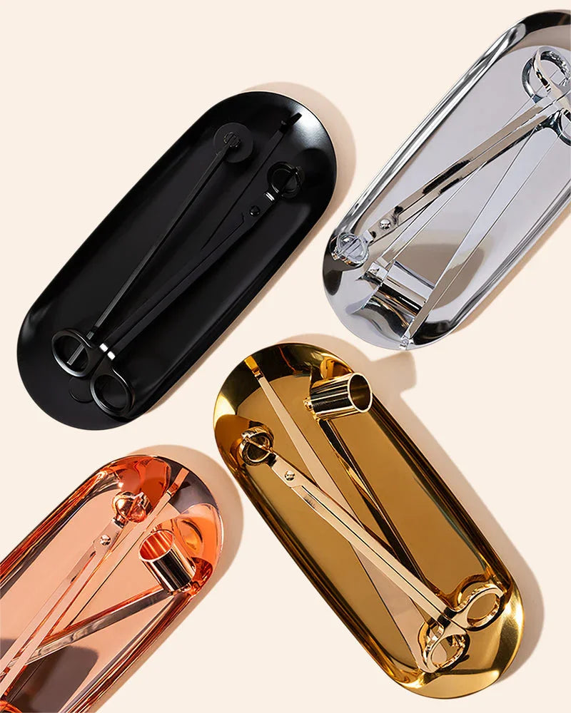 Four Makesy® Candle Care Kits in black, silver, rose gold, and gold are neatly arranged on oval trays. Each kit includes scissors, a wick trimmer, and other tools displayed on a light background.