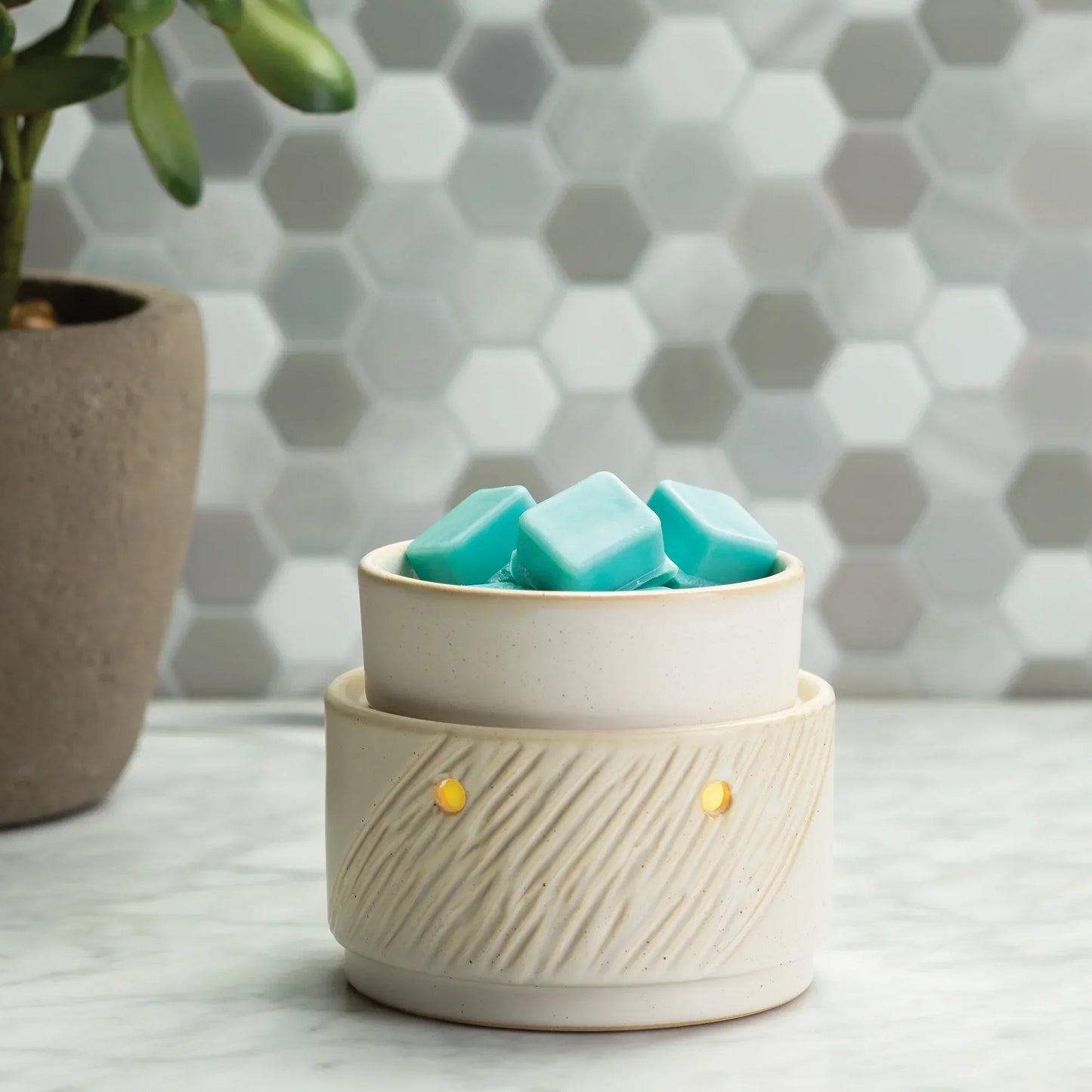 Ceramic wax melt warmer with blue wax melts on marble countertop, hexagonal tile background