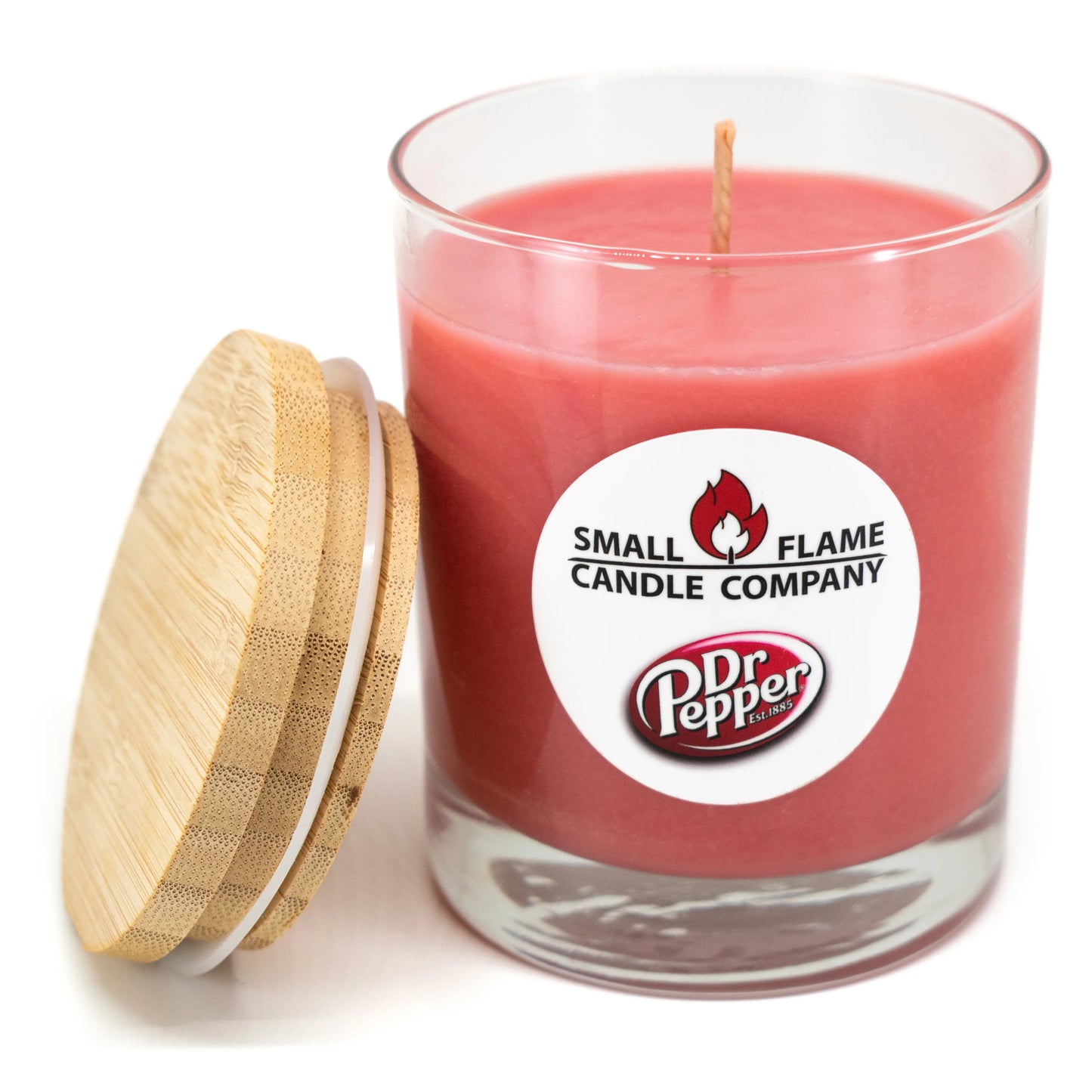 A pink Dr Pepper Candles and Melts product in a clear glass jar with wooden lid, made from coconut soy wax and natural fragrance oils. A white label reads Small Flame Candle Company and Dr Pepper; an unlit wick sits at the center.