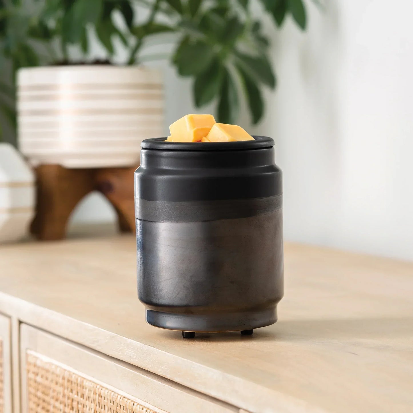 Black ceramic wax melt warmer with yellow wax cubes on a wood surface, indoor setting
