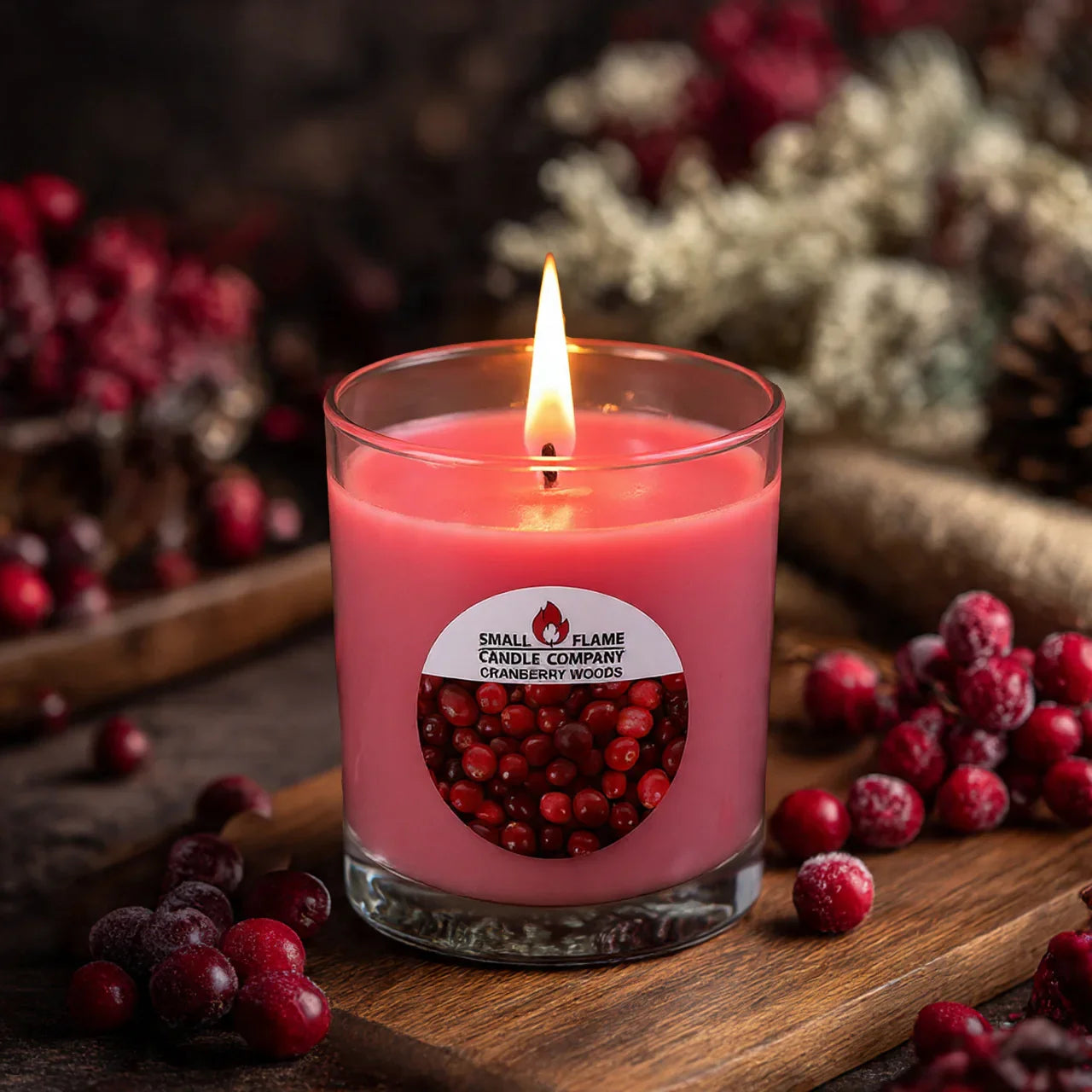 Pink Cranberry Woods candle in glass jar, lit, surrounded by fresh cranberries on a wooden table