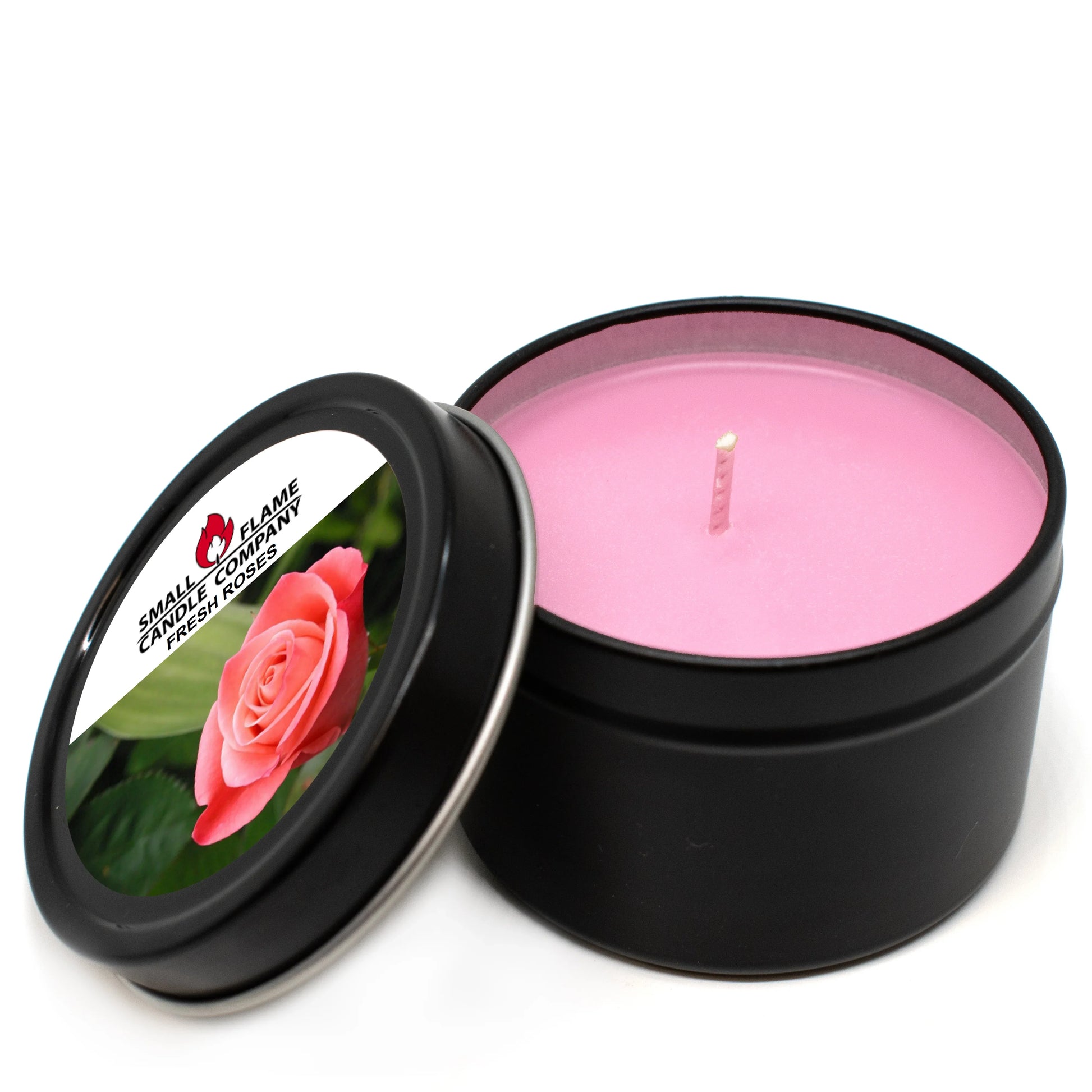 Pink rose scented candle in black tin with rose label and lid beside candle.