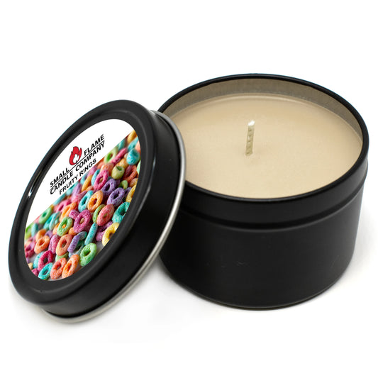 A black metal tin Fruity Rings Candle with its lid off displays a label featuring colorful fruit cereal rings and “FRUIT CIRCLES.” The beige coconut soy wax candle from Fruity Rings Candles and Melts has a centered wick.