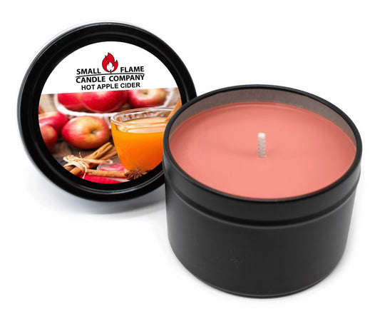 A black tin Hot Apple Cider Candles and Melts from Small Flame Candle Company with red coconut soy wax and natural fragrance oils. The label features apples, cinnamon sticks, and cider; the lid sits beside the open candle.
