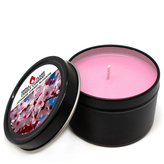 A black tin coconut soy wax candle from Small Flame Candle Company’s Japanese Cherry Blossom Candles and Melts features a pink center, a lid with cherry blossom art, and a label. Crafted with natural fragrance oils for a delightful scent experience.