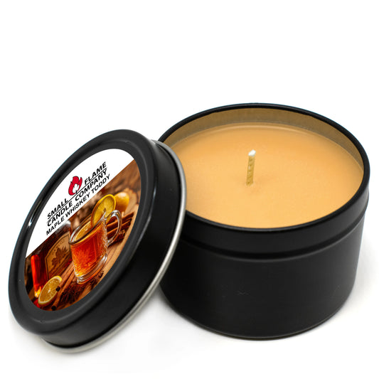 The Small Flame Candle Company Maple Whiskey Toddy Candles feature a round black tin, beige coconut soy wax, a single wick, and a lid with whiskey glasses, cinnamon sticks, citrus slices, and product name. Made with natural fragrance oils.