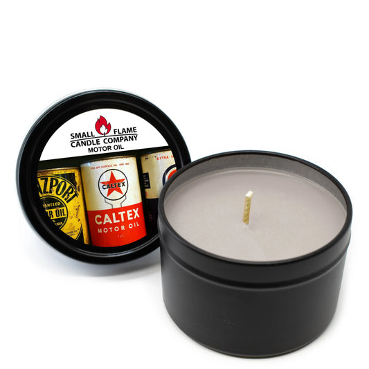 A black tin Motor Oil Candles and Melts hand-poured candle with gray coconut soy wax, a lid featuring vintage motor oil can designs, and labeled by Small Flame Candle Company.