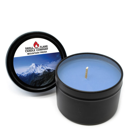 A black tin from Small Flame Candle Company holds a Mountain Fresh candle, its blue wax made with coconut soy and natural fragrance oils. The lid shows a snowy mountain and the Mountain Fresh Candles and Melts name.