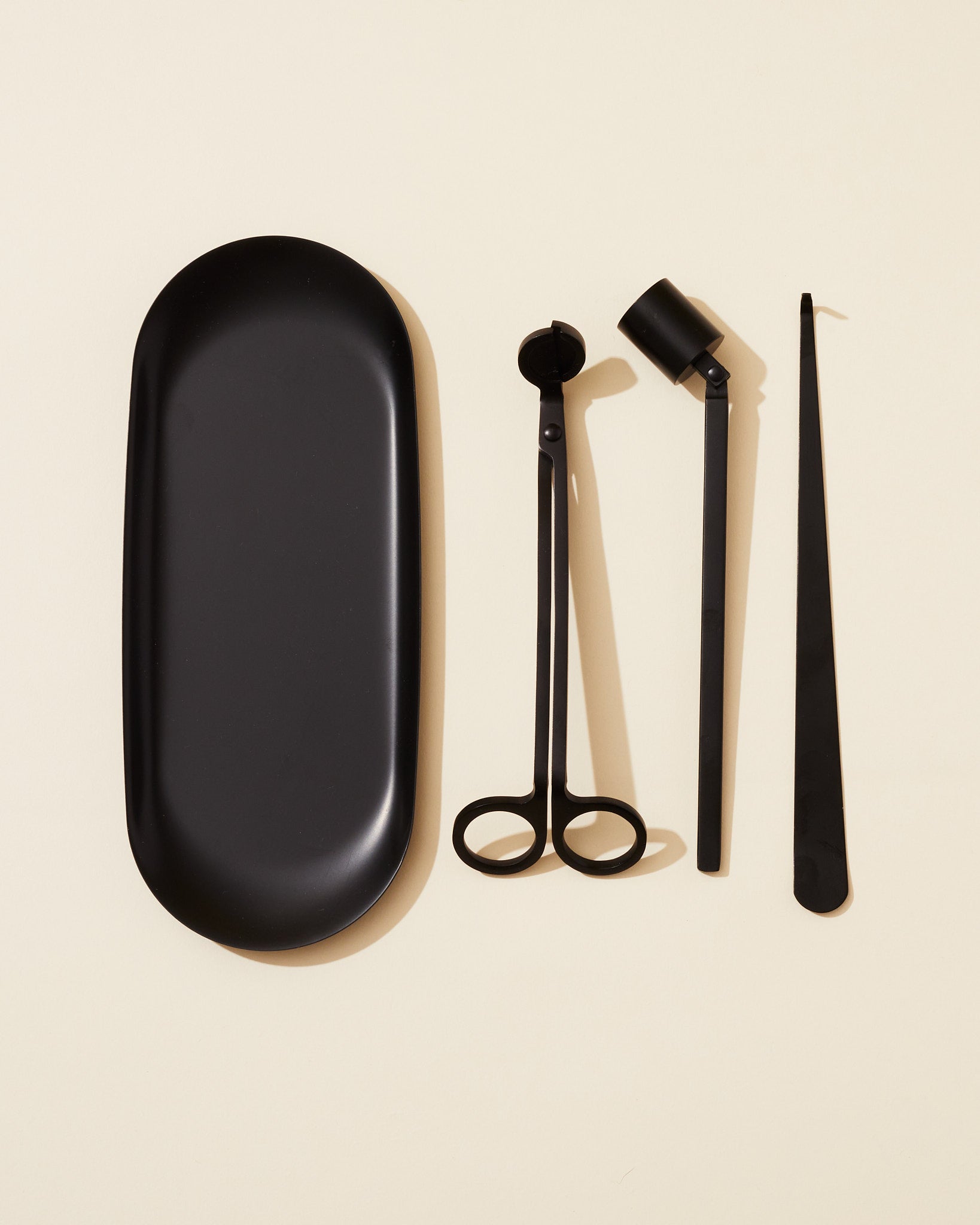 The Makesy® Candle Care Kit, in black metal, includes a tray, wick trimmer, snuffer, and wick dipper arranged side by side on a light beige background.