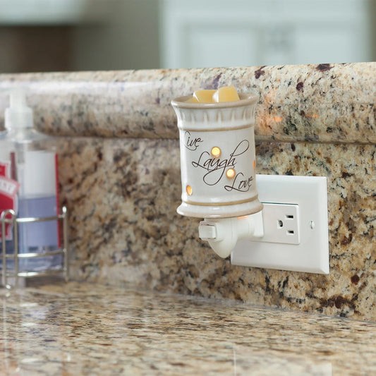 The Live, Laugh, Love Pluggable glows warmly on a granite kitchen counter, filled with wax melts. Plugged into an outlet, it adds ambiance and charm to your kitchen décor among everyday essentials.