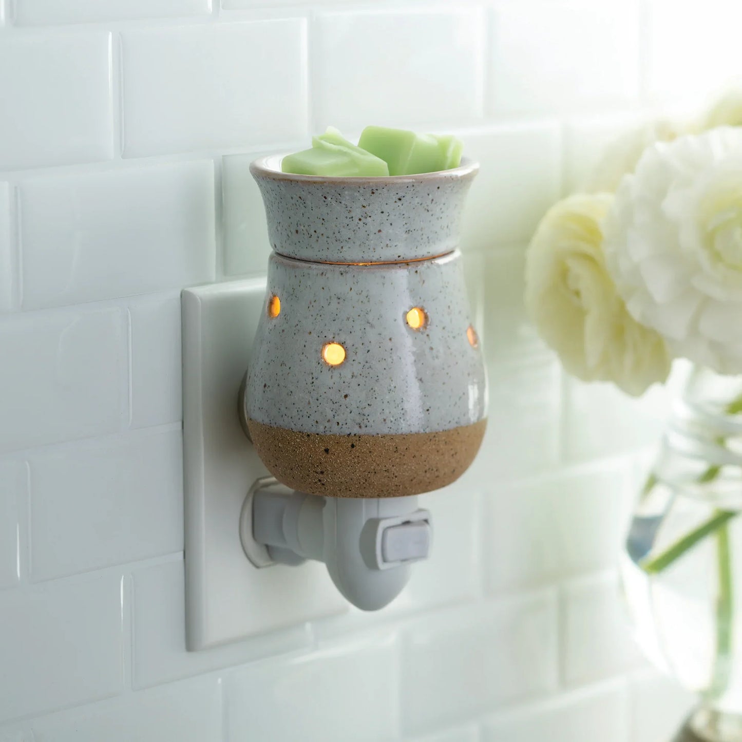 Rustic white ceramic pluggable wax warmer with glowing lights and green wax melts