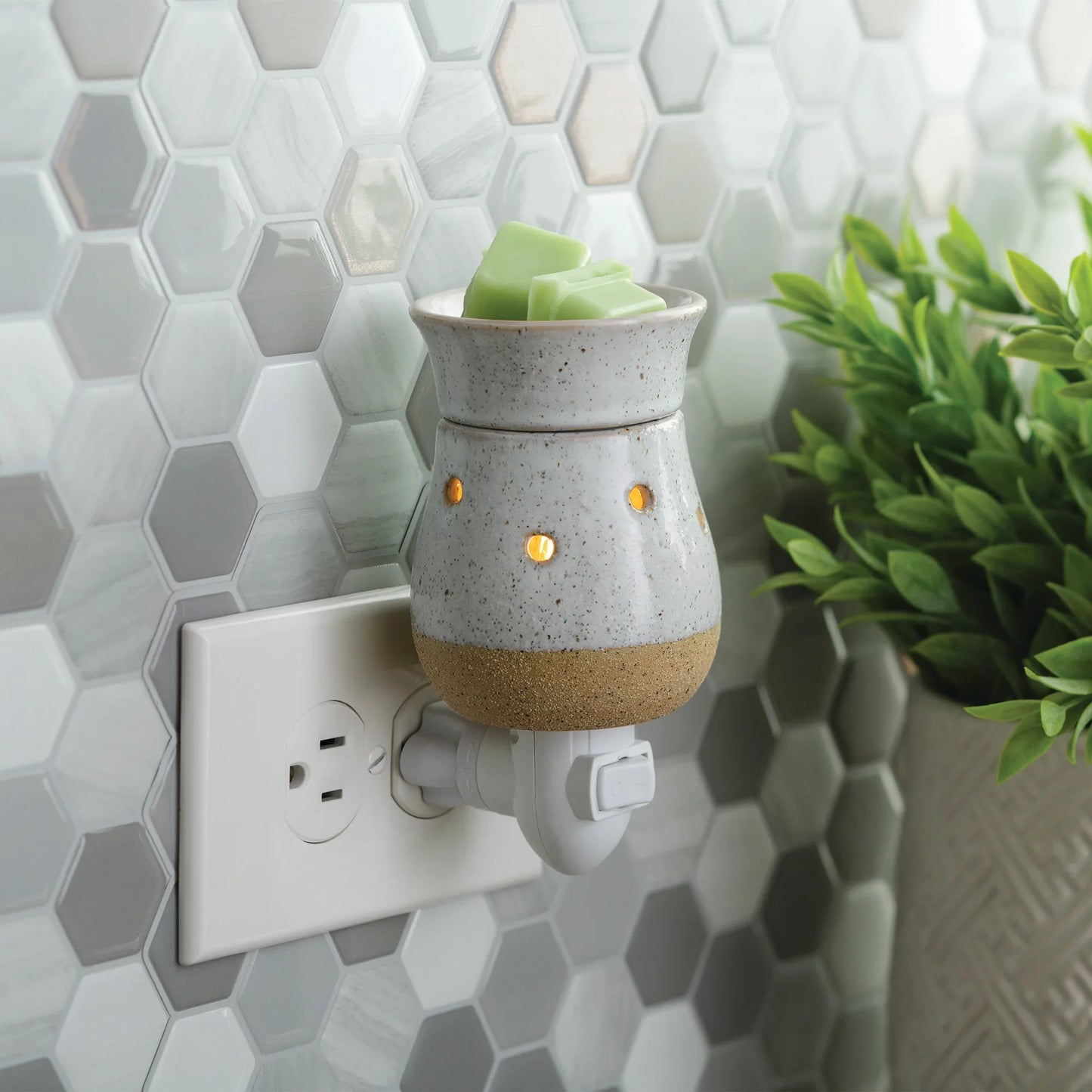 Rustic ceramic plug-in wax melt warmer with green wax cubes in a modern kitchen setting.