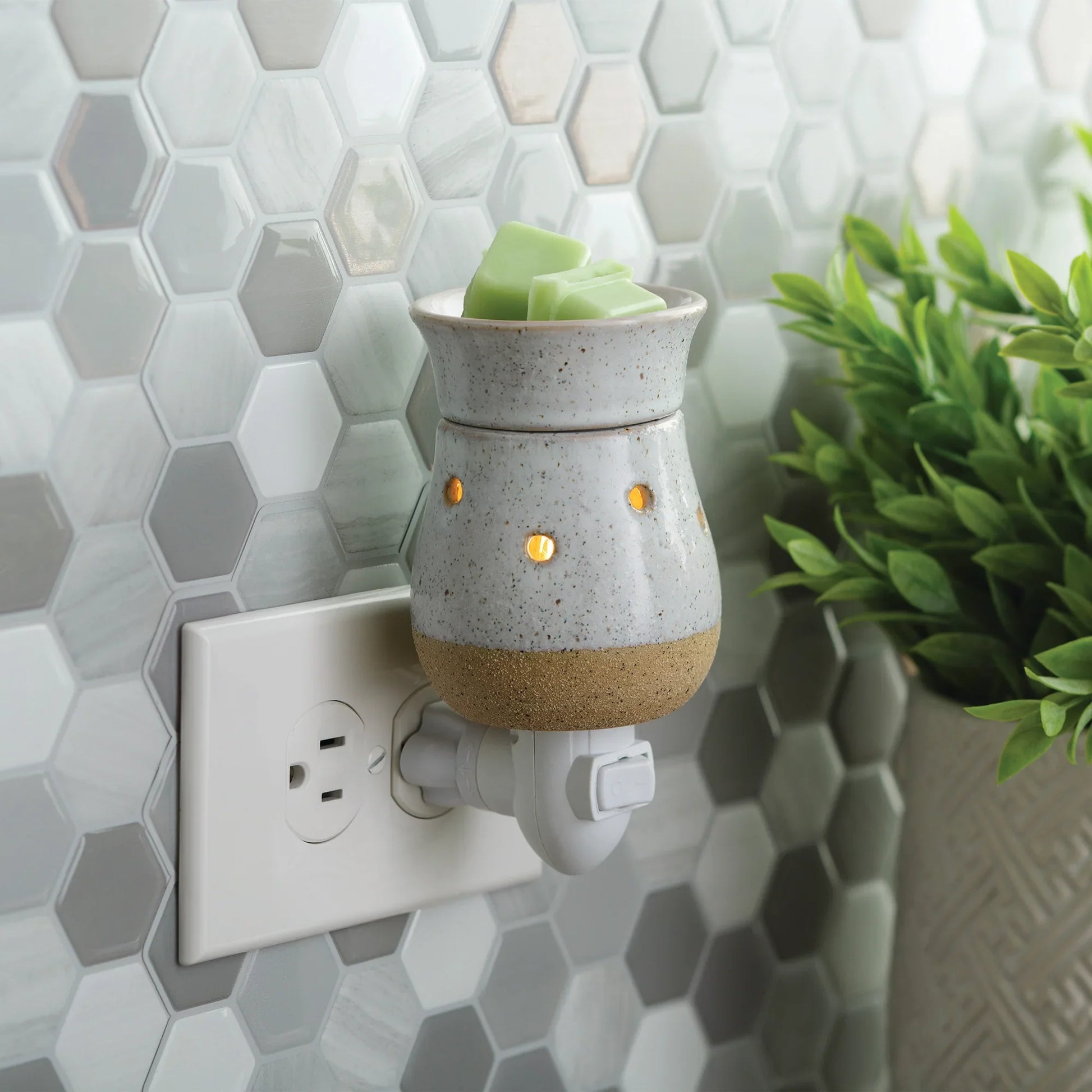 Rustic ceramic plug-in wax melt warmer with green wax cubes in a modern kitchen setting.